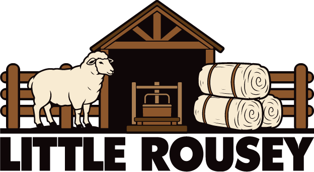 Little Rousey design: A woolly sheep standing beside a timber shearing shed and round hay bales behind a wooden fence, above bold black "LITTLE ROUSEY" text.